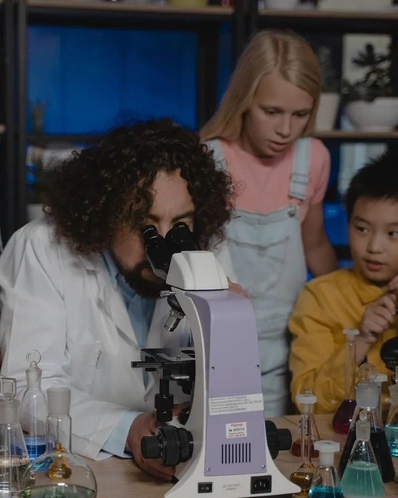 Children crowd around a microscope, leaning in to see